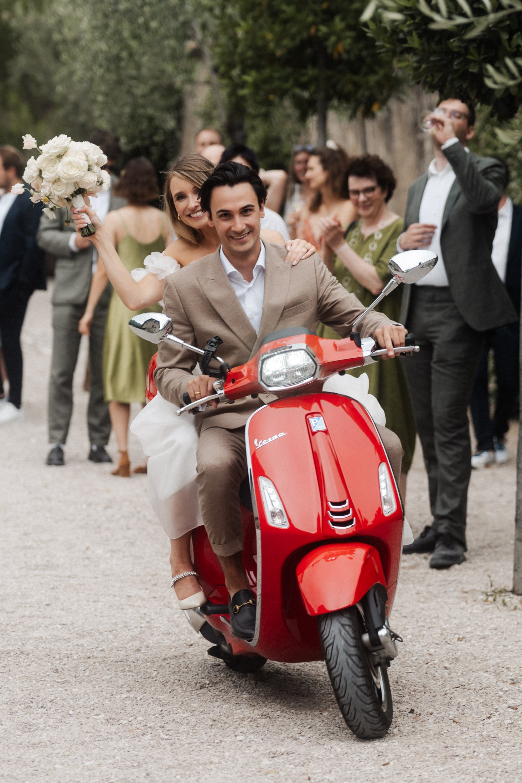 Brautpaar fährt auf einer Vespa davon, die Braut winkt